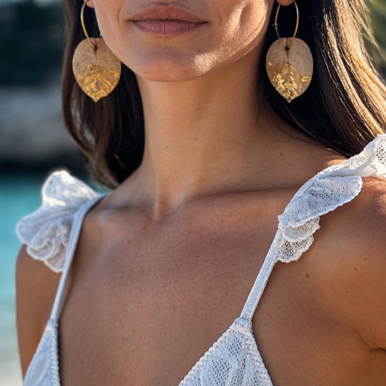 Woman in a white bikini standing on a beach with turquoise water and greenery in the background