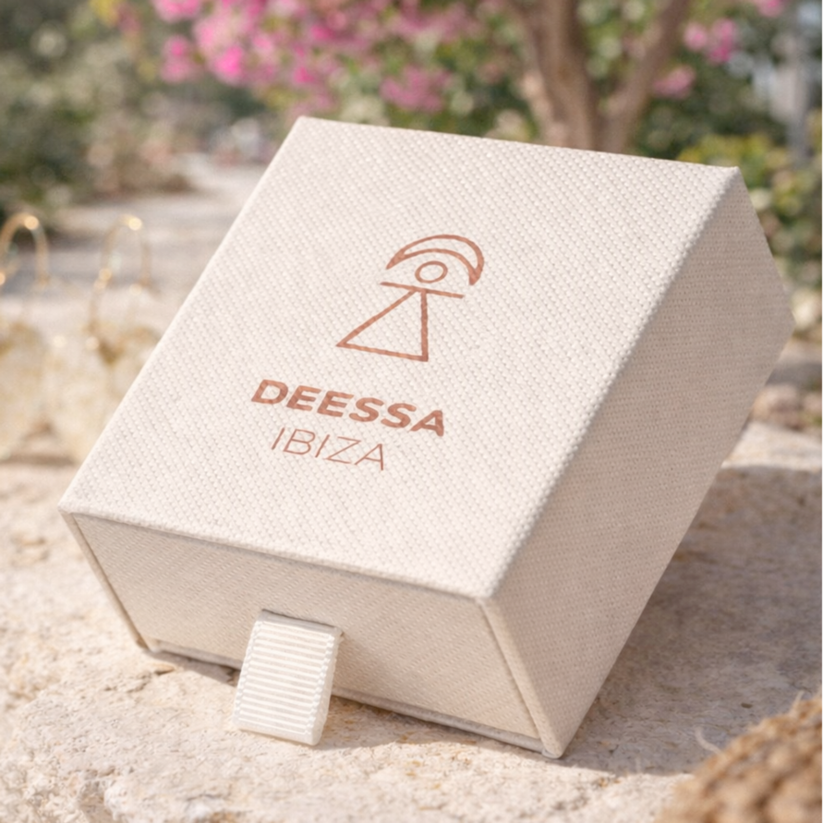 Deessa Ibiza jewelry box on a stone surface with pink flowers in the background